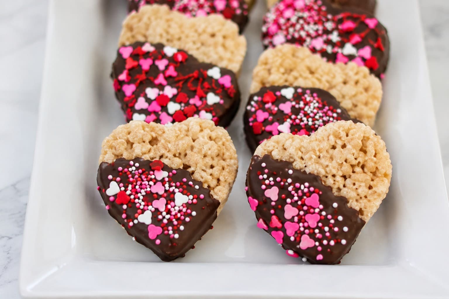 Heart-shaped Rice Krispie treats dipped in chocolate and decorated with pink sprinkles
